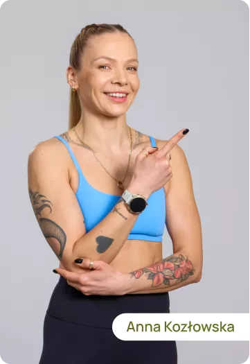 Smiling woman in a blue sports bra points to the right; has tattoos and a smartwatch on her wrist.
