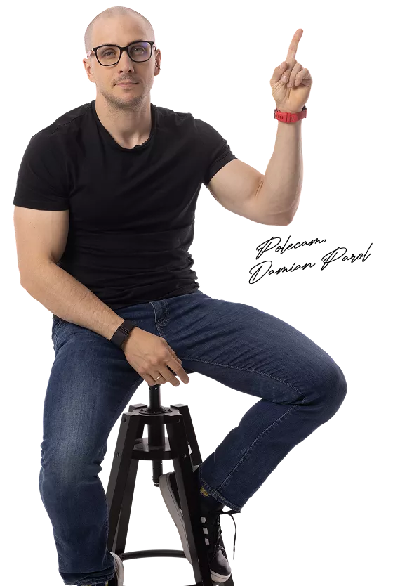 Man wearing a black t-shirt and glasses sits on a stool, raising his right index finger as if signaling 'one' or drawing attention upward.