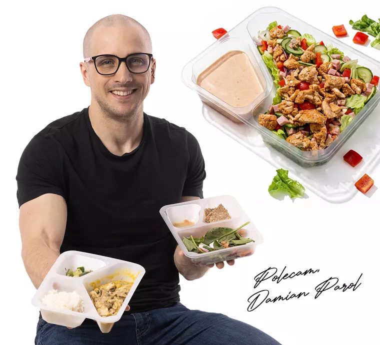 Smiling man in a black T‑shirt holds two meal-prep containers with salad and a dressing cup, against a white background, with a larger meal bowl in the corner.