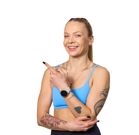 Fit woman in a blue sports bra points to the left with a smile, showing tattoos on her arms and a smartwatch.